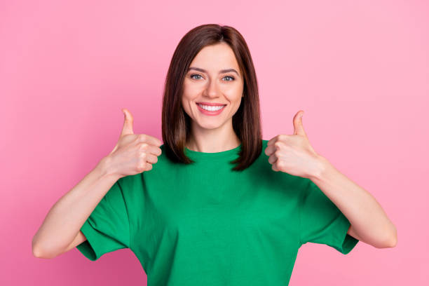 foto de joven feliz linda mujer bonita sostiene pulgares hacia arriba recomendar nuevo blanqueamiento estomatológico aislado sobre fondo de color rosa - young women smiling women human teeth fotografías e imágenes de stock