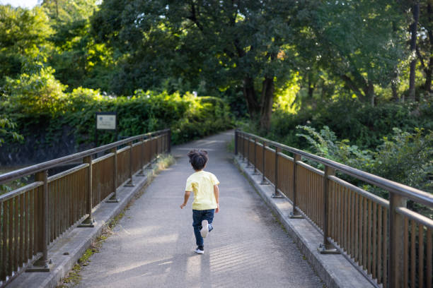 Japanese family visiting public park by bicycle to enjoy walking in forest, playing with ball and equipments, eating foods.