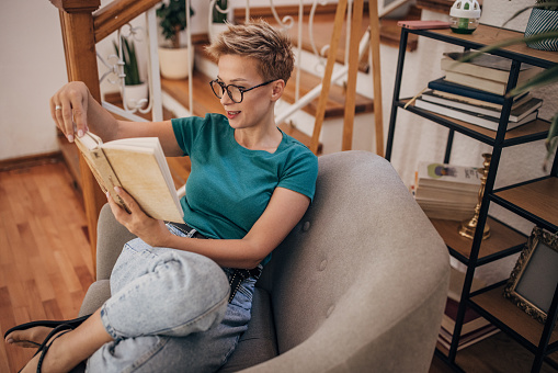 Beautiful shorthaired woman relaxing on armchair at home, she is reading a book.