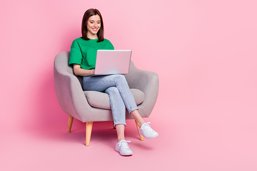 Full length portrait of cheerful pretty person sit chair use wireless netbook isolated on pink color background.