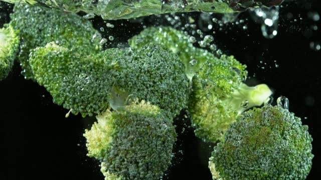 Super slow motion of falling broccoli into water.