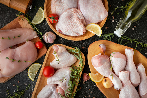 Raw uncooked chicken meat on a wooden cutting board with spices and herbs. Top view of chicken thigh, leg, fillet and wings on the black background.