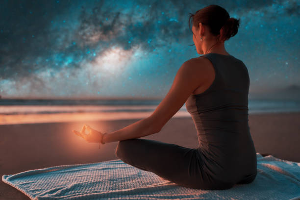 silhouette of a woman on the beach outdoors meditating at night with stars and milky way in the background stock photo