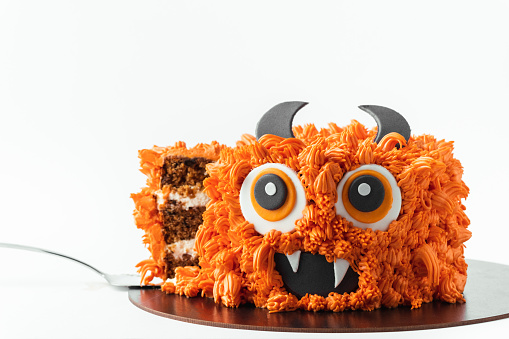 Monster theme cake on the white background. Halloween cake with orange fluffy cream cheese frosting isolated on white