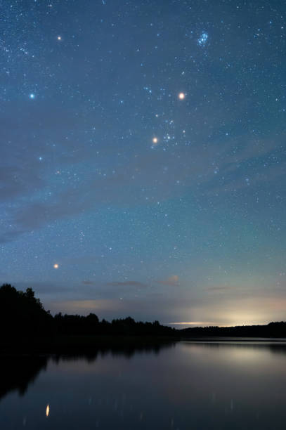 Autumn night landscape under starry sky. Stars reflecting from calm water surface.