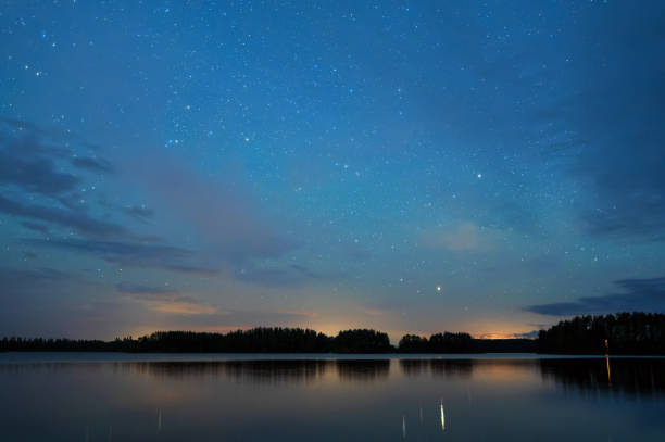 istock Night landscape under starry sky, stars reflecting from calm water surface, distant thunder in the horizon. 1425214317