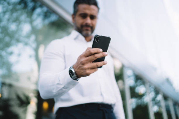 Below view of blurred businessman connecting to wireless for browsing banking application on modern smartphone device, male downloading files and texting via selective mobile gadget with 4g internet