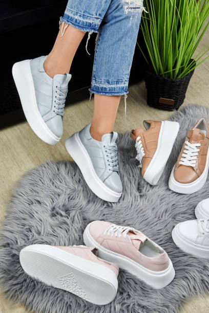 Young woman in blue jeans trying on gray sport shoes on fur rug in shop, copy space. Woman wearing comfortable stylish sneakers indoors, closeup stock photo