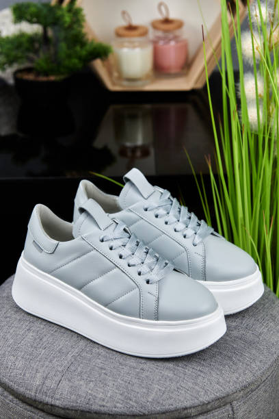 Stylish gray female shoes on gray pouf background in shop, copy space. New sneakers, close up. Beauty and fashion concept. stock photo