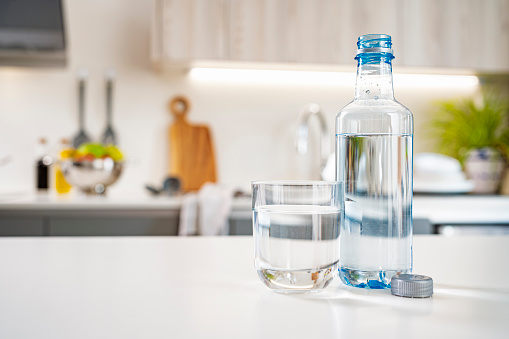 Close up view of an open plastic water bottle and drinking glass shot on kitchen counter. Selective focus on foreground. Copy space. High resolution 42Mp indoors digital capture taken with Sony A7rII and Sony FE 90mm f2.8 macro G OSS lens