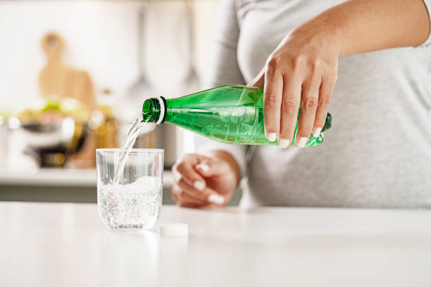 Pouring mineral water from green plastic bottle in glass Close up view of female hands pouring tonic water from a green plastic bottle to a glass on kitchen counter. High resolution 42Mp indoors digital capture taken with Sony A7rII and Sony FE 90mm f2.8 macro G OSS lens pouring water from bottle stock pictures, royalty-free photos & images