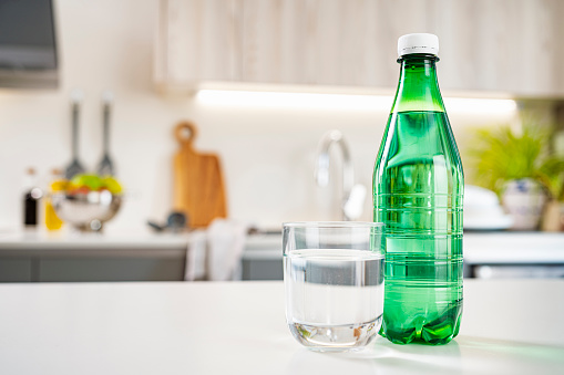 Close up view of a green plastic tonic water bottle and drinking glass shot on kitchen counter. Selective focus on foreground. High resolution 42Mp indoors digital capture taken with Sony A7rII and Sony FE 90mm f2.8 macro G OSS lens