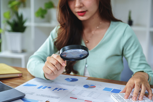 A half-bred girl, an audit employee, an accountant holding a magnifying glass and using a calculator to check the financial statement documents to calculate the annual tax payment to the IRS.