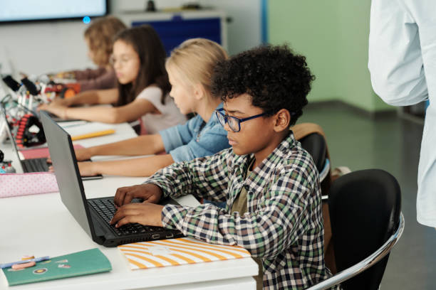 Side view of youthful African American schoolboy working in front of laptop stock photo