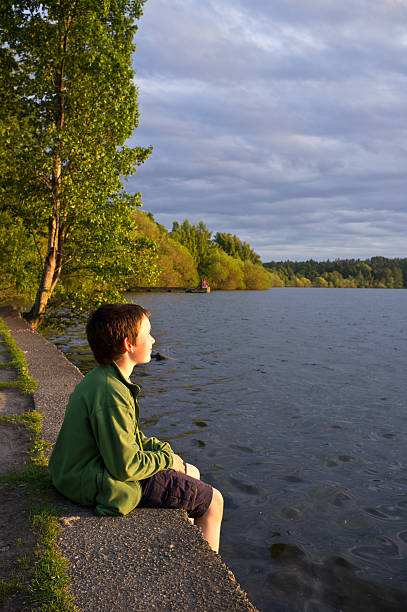 Young boy watching sunset at lake side stock photo