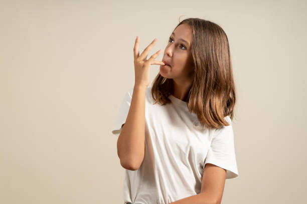 베이지 색 스튜디오 배경에 고립 된 맛있는 것을 먹은 후 손가락을 빨아 먹는 라틴 십대 소녀의 초상화. - finger licking 뉴스 사진 이미지
