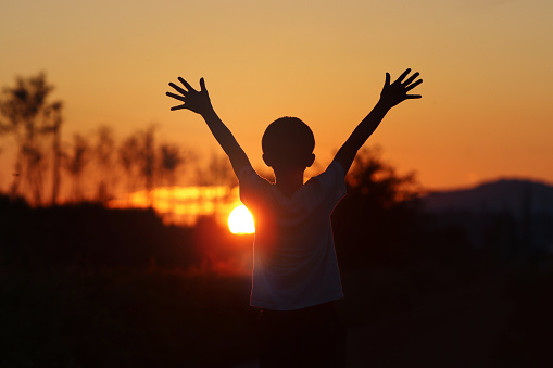 Dream and hope, challenge and success freedom concept silhouette with child with arms outstretched towards the sun at sunset landscape