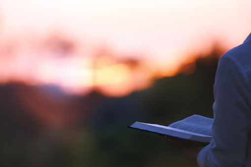 Un cristiano orando mientras mira el sol poniente y la Santa Biblia photo