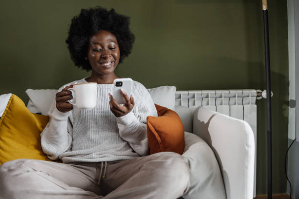 A young African-American woman drinking morning coffee and checking social media stock photo