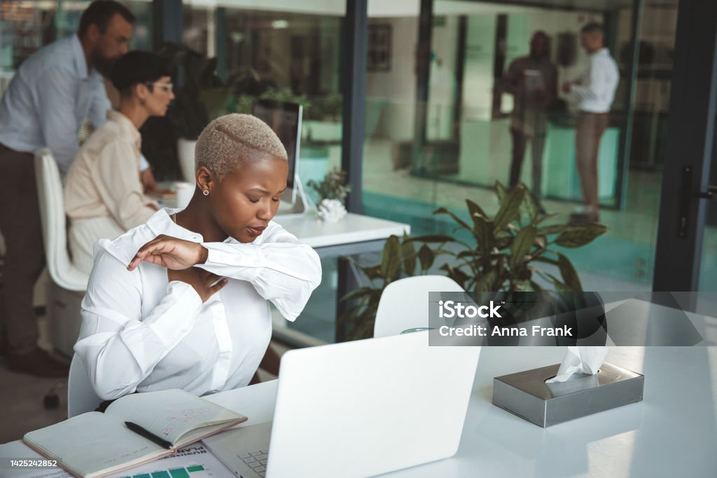 I don't have time to be sick Shot of a young businesswoman coughing and holding her hand on her chest while working in a modern office Office Stock Photo