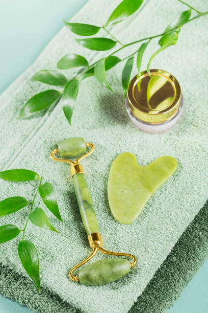 istock Green jade face roller and gua sha scraper with leaves on light blue background 1425246303