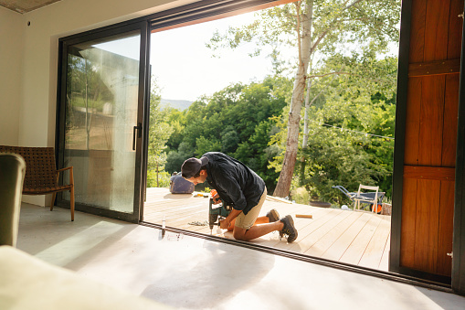 Photo of a carpenter installing wooden decking in front of a cabin house