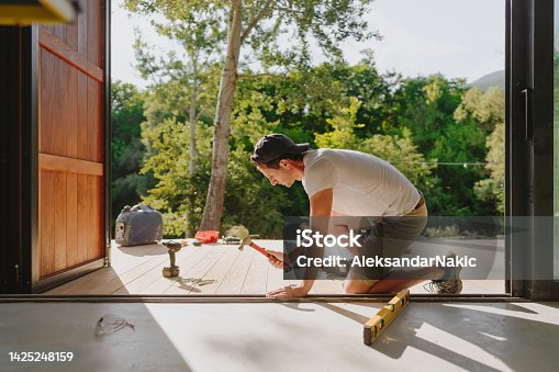 istock Man working on wooden decking in front of a cabin house 1425248159
