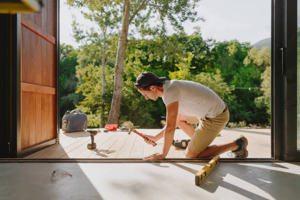 Man working on wooden decking in front of a cabin house Photo of a carpenter installing wooden decking in front of a cabin house decking stock pictures, royalty-free photos & images