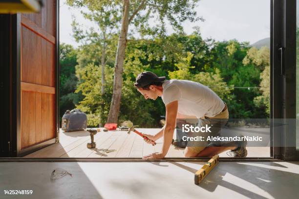 Man Working On Wooden Decking In Front Of A Cabin House Stock Photo - Download Image Now