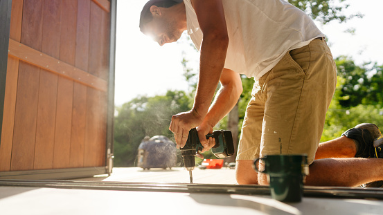 Photo of a man installing wooden decking in front of a cabin house
