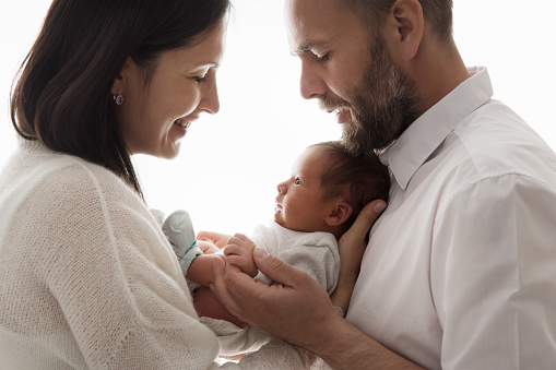 Family with Newborn Baby. Happy Parents holding one month Child. Smiling Mother and Father Silhouette with Infant over White Studio Background. Parenting Love and Childcare