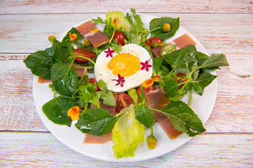 Recipe Fried egg on a bed of salad with Mafane, rocket, cherry tomato, cured ham and a balsamic dressing. High quality photo