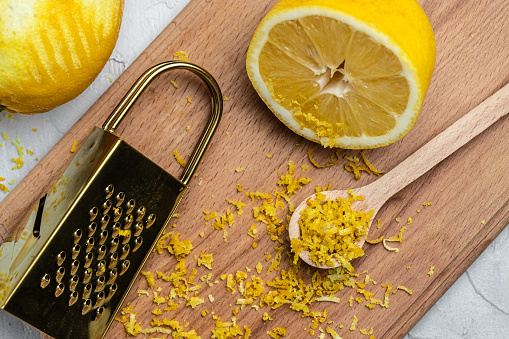 Peeling lemon rind to add zest to Mediterranean recipes. Grater peel and lemon zest on light background, place for text, top view.