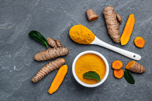 turmeric powder in spoon with turmeric root. curcuma or curcumin on concrete background. Spice, natural coloring, alternative medicine. Long banner format. top view.