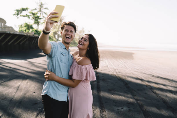 Joyful expecting couple taking selfie on beach