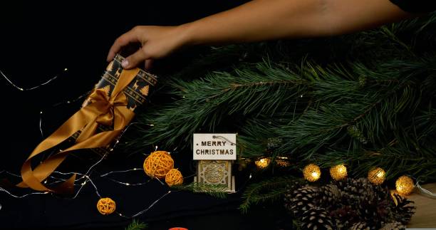 한 여성이 화환과 장난감으로 크리스마스 트리 아래에 아름답게 포장 된 선물을 놓습니다. 크리스마스 이브에는 모든 사람들이 크리스마스와 새해 선물의 크리스마스 트리 개념 아래에 선물을  - new years eve christmas paper christmas fir tree 뉴스 사진 이미지