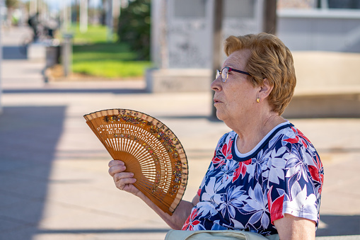 Close portrait, older woman fanning herself on a hot day, sitting on a bench in the city