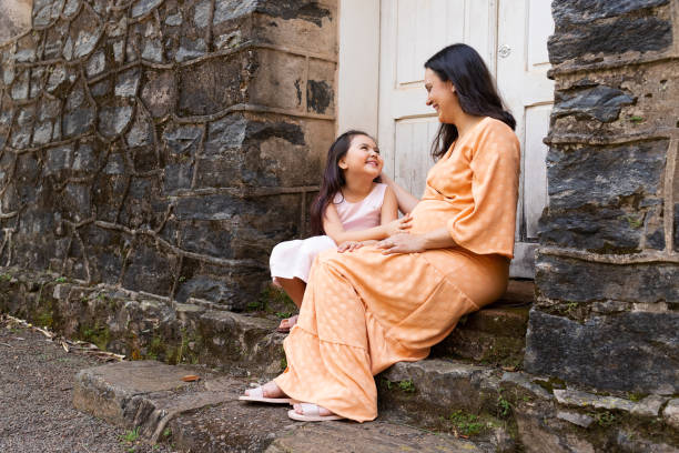 Pregnant mother and her daughter smiling at each other. Multiracial family. Mixed race Japanese little girl and latin American mother