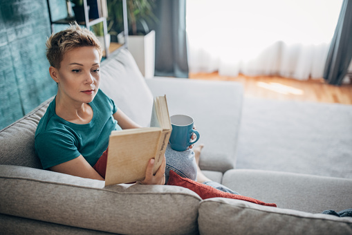 Beautiful shorthaired woman relaxing on sofa at home, she is reading a book.