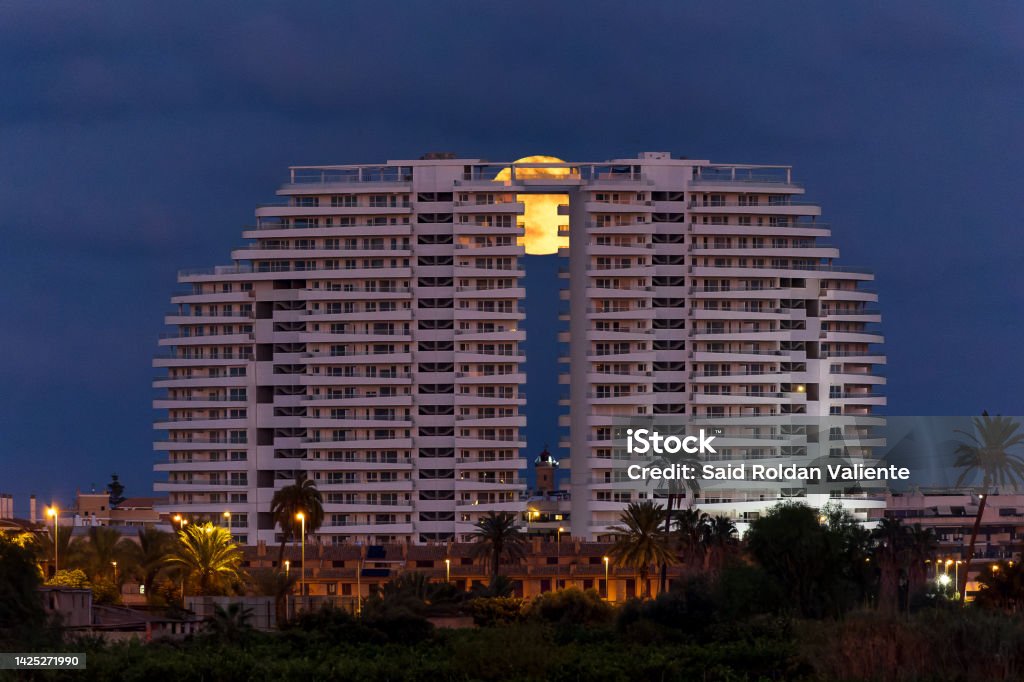 View of the Gran Canet building, with the full moon behind and the lighthouse of Canet de Berenguer in the middle Apartment Stock Photo
