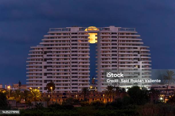 View Of The Gran Canet Building With The Full Moon Behind And The Lighthouse Of Canet De Berenguer In The Middle Stock Photo - Download Image Now