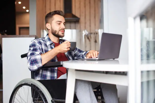 Photo of Young man in wheelchair working on laptop fromhome