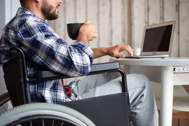 Photo of Young man in wheelchair working on laptop fromhome