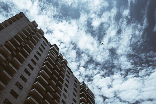 View from the bottom of a residential house elevation with plenty of balconies and windows, beautiful blue sky texture with cloudscape, and the silhouette of a helicopter flying by