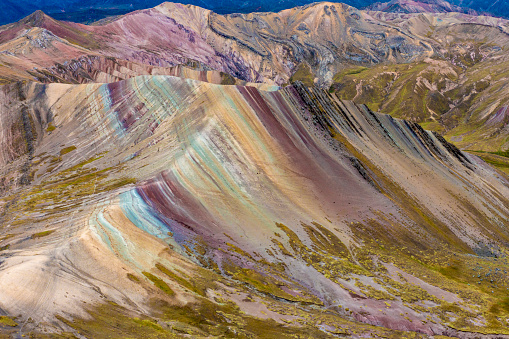 Palcoyo Rainbow Mountain, Cusco, Peru - August 27, 2022; In Palcoyo there are three Rainbow Mountains. The Rainbow Mountains are composed of stratified layers of sandstone. These fine-grained rock layers contain large amounts of iron and other minerals, which give the mountains the pigments for the various colored stripes

From Palcoyo it's possible to see the glacial Ausangate Peak. Palcoyo is also famous for its stone forest area which is 4900 metres above sea level. The name is given due to the look of the big standing sharp stones that gives the illusion of a forest.