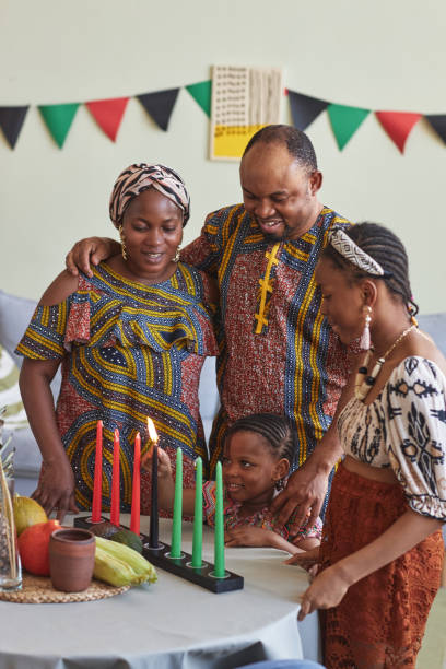 African family of four celebrating Kwanzaa African family of four embracing and smiling while little girl burning candles for Kwanzaa holiday angolan kwanza photos stock pictures, royalty-free photos & images