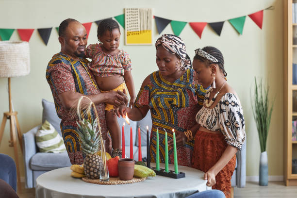 African family of four celebrating Kwanzaa at home African family of four celebrating Kwanzaa at home, they lighting seven candles together on table angolan kwanza photos stock pictures, royalty-free photos & images