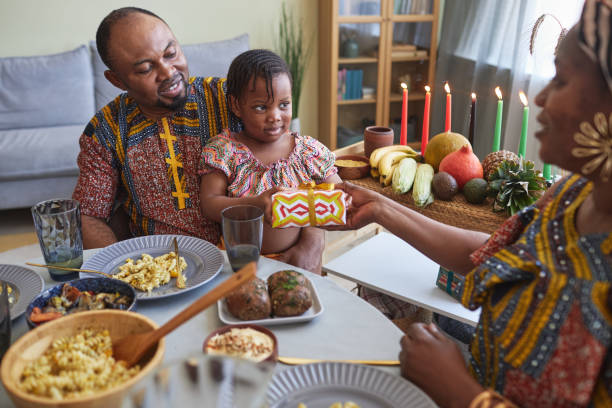 Parents giving present to their daughter African parents giving present to their little daughter for holiday while they sitting at dining table angolan kwanza photos stock pictures, royalty-free photos & images