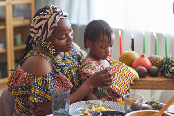 Mom opening gift with her child African woman in national costume opening present with her little daughter while they sitting at dining table angolan kwanza photos stock pictures, royalty-free photos & images