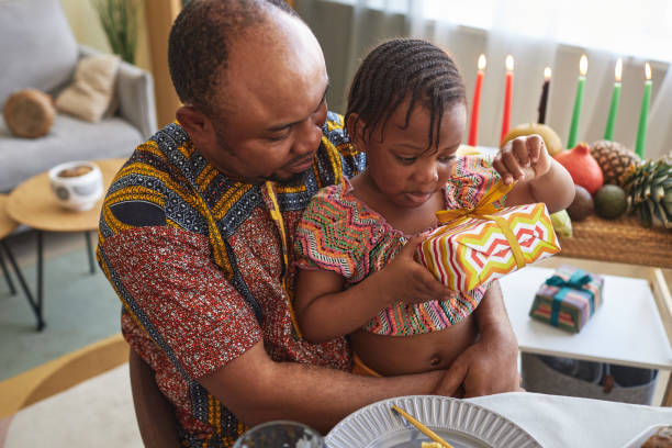 Little girl opening gift box African little girl opening gift box while sitting on knees of her father at dining table angolan kwanza photos stock pictures, royalty-free photos & images